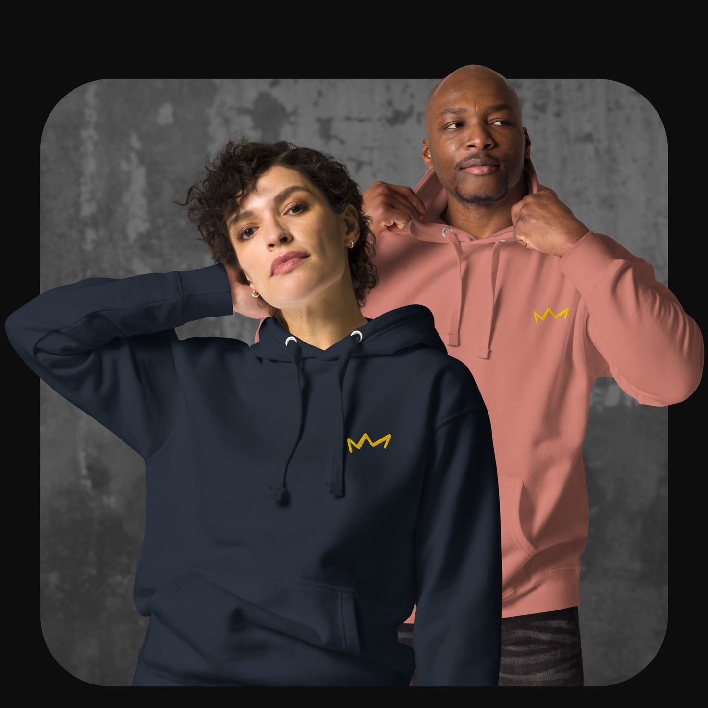 Frau in dunkelblauem Hoodie und Mann in rosafarbenem Hoodie, beide mit gelber Krone auf der linken Brust. Hintergrund in Betonoptik.