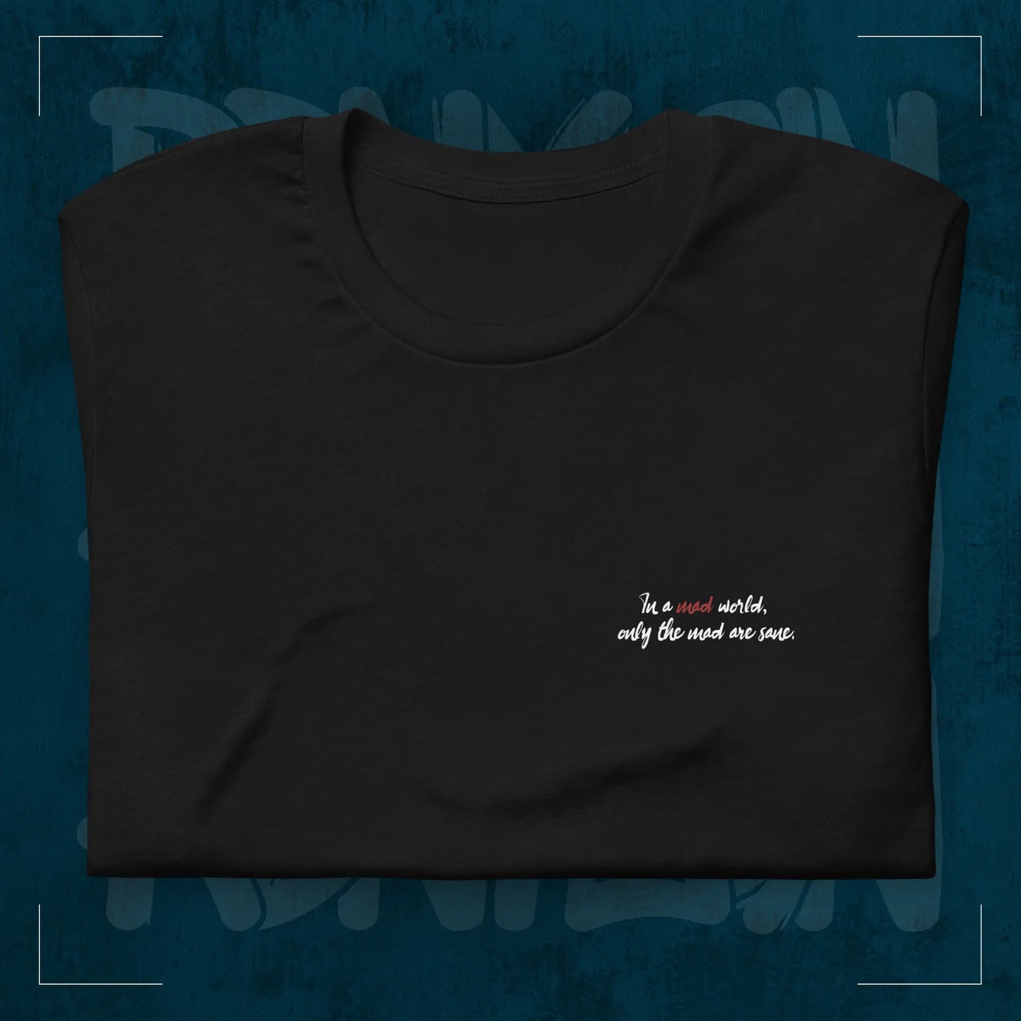 Schwarzes RodneyLogan Regular T-Shirt mit kleinem „Welcome to the Madhouse“-Brustprint als Detailaufnahme auf dunkelblauem Hintergrund.