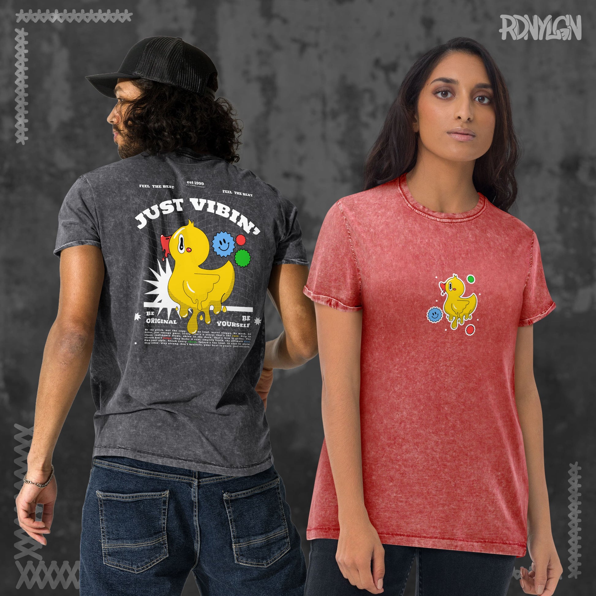 Eine Frau trägt ein rotes Acid-Wash-T-Shirt mit kleinem Entchen vorne. Neben ihr ein Mann mit schwarzem Acid-Wash-T-Shirt, das auf der Rückseite ein großes Entchen-Motiv mit dem Schriftzug „JUST VIBIN’ – Be Yourself“ zeigt.