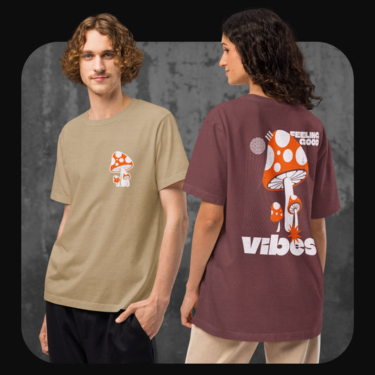 Ein Mann trägt ein beigefarbenes T-Shirt mit kleinem roten Fliegenpilz-Print auf der Brust, daneben eine Frau mit weinrotem T-Shirt und großem Rückendruck eines Fliegenpilzes mit Schriftzug „Feeling Good Vibes“.