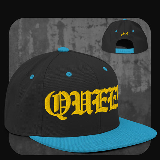 Schwarze Snapback-Cap mit leuchtend blauer Krempe, blauen Ösen und Knopf. Gelber Schriftzug „QUEEN“ in Frakturschrift auf der Vorderseite, gelbe Krone auf der Rückseite.
