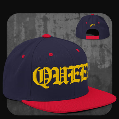 Dunkelblaue Snapback-Cap mit roter Krempe, roten Ösen und rotem Knopf. Gelber „QUEEN“-Schriftzug auf der Vorderseite, gelbes Kronenlogo hinten.