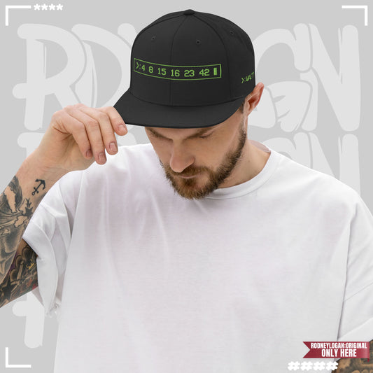 Person mit tätowiertem Arm trägt schwarze Cap mit grünem Stick und grauem Schirm, vorne mit der Zahlenreihe „4 8 15 16 23 42“ und seitlich „>: WALT?“. Keywords: Cap, Snapback, schwarz, Stickerei, Terminal Design, Lost Zahlen, Accessoire.