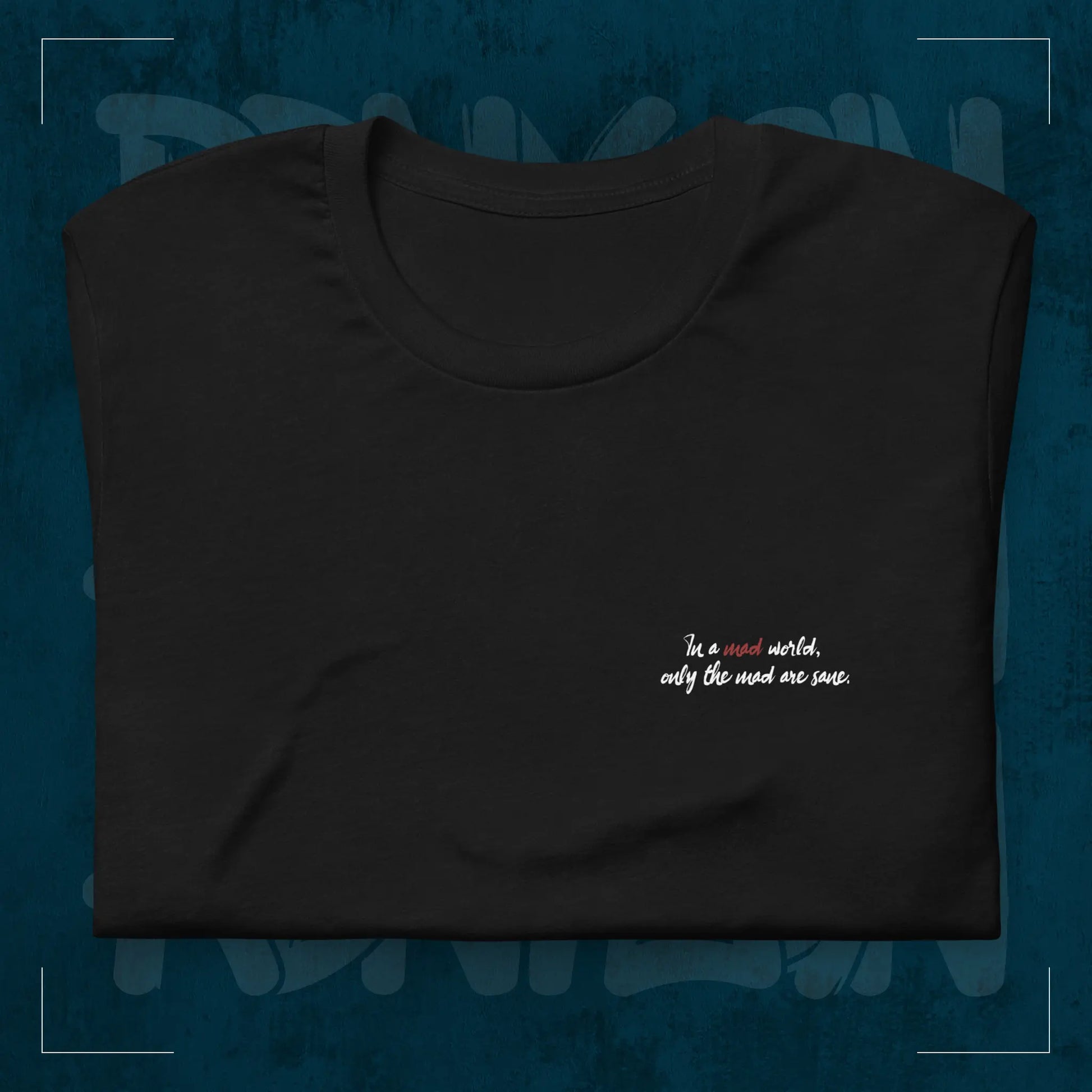 Schwarzes RodneyLogan Regular T-Shirt mit kleinem „Welcome to the Madhouse“-Brustprint als Detailaufnahme auf dunkelblauem Hintergrund.