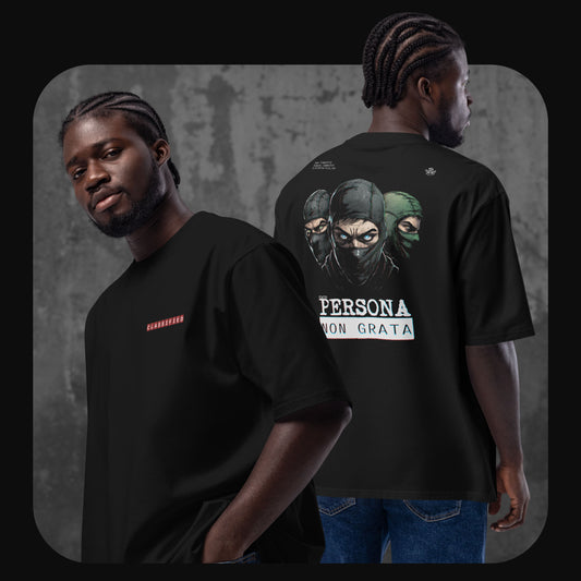 Man wearing a black oversized t-shirt with a red “CLASSIFIED” label on the front and a large illustrated graphic on the back showing three masked figures and the text “PERSONA NON GRATA.”