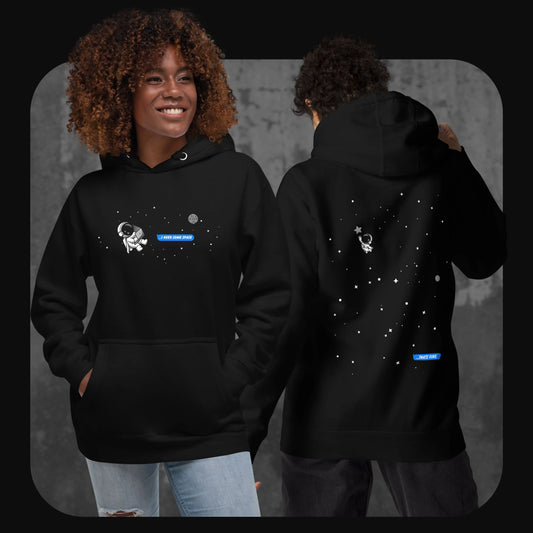 Lifestyle image showing two models wearing the black “I Need Some Space” hoodie – one facing forward with the astronaut and message on the chest, the other turned around revealing the back design with stars and the distant astronaut.