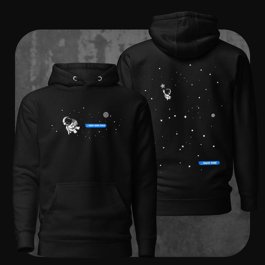 Image of a black hoodie with a small astronaut floating in space and a blue text bubble on the front reading “I need some space”, and on the back the same astronaut drifting further away with a reply bubble saying “That’s fine”.