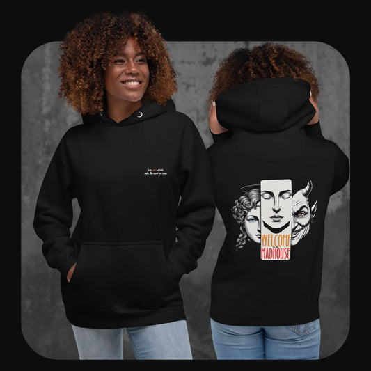 Two models wearing the same black hoodie; the front shows minimalist text while the back reveals a bold and artistic face trio design centered around the phrase “Welcome to the Madhouse”.