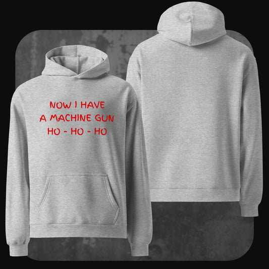 A light grey hoodie with red handwritten-style text on the front that reads “NOW I HAVE A MACHINE GUN HO - HO - HO.” The back of the hoodie is plain with no design.
