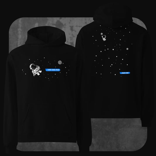 Front and back view of a black oversized hoodie featuring a minimalist outer space theme. The front shows a small cartoon astronaut floating in space with the text bubble “I NEED SOME SPACE” in blue. The back displays the astronaut drifting farther among stars with a reply bubble that says “THAT’S FINE” also in blue.